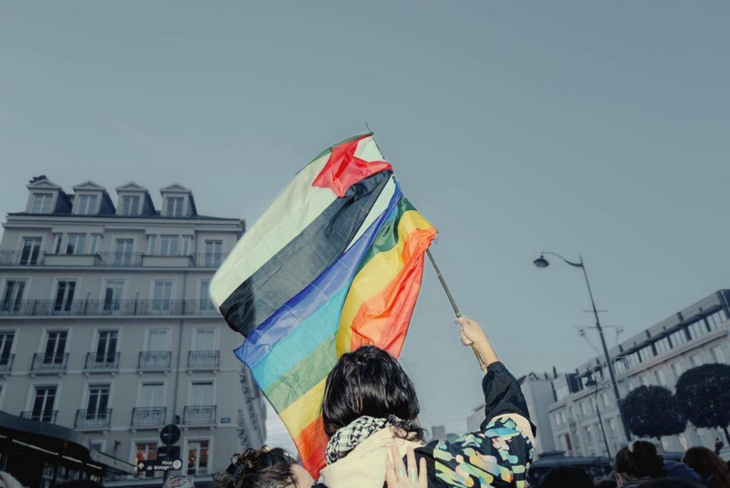 Une personne brandissant deux drapeau :  un drapeau LGBT et un drapeau palestinien